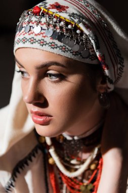 portrait of young ukrainian woman in traditional headwear with ornament and red beads on black  clipart