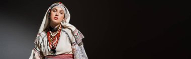young ukrainian woman in traditional clothing with ornament and red beads on black, banner