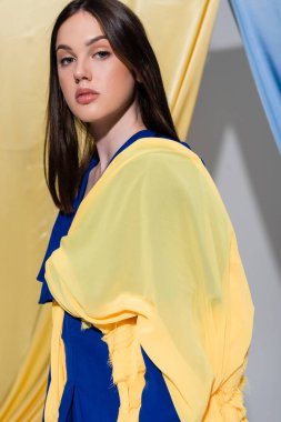 young ukrainian woman in color block clothing posing near blue and yellow curtains  clipart