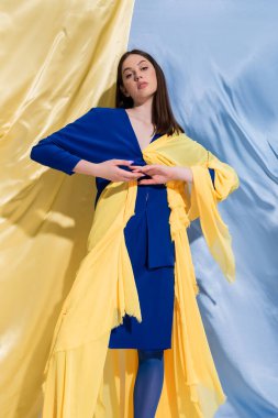 confident young ukrainian woman in color block clothes posing near blue and yellow curtains 