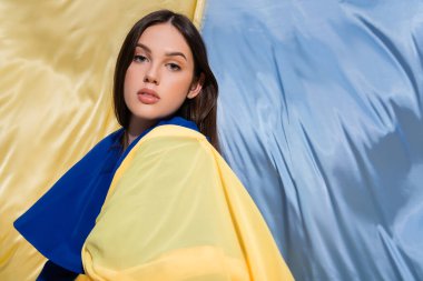 patriotic young ukrainian woman in color block clothing posing near blue and yellow flag