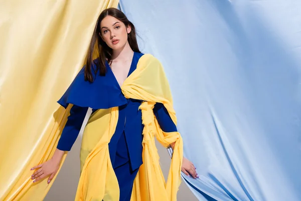 young ukrainian woman in color block dress looking at camera near blue and yellow curtains