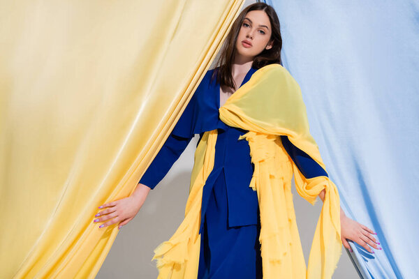 stylish young ukrainian woman in color block dress posing near blue and yellow curtains 