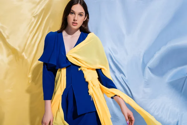 Молодая Украинка Цветной Блочной Одежде Позирует Возле Синей Желтой Ткани — стоковое фото