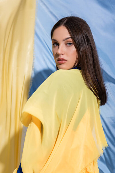 young ukrainian woman in yellow clothing posing near national flag 