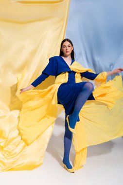 full length of young ukrainian woman in stunning color block clothing posing near blue and yellow fabric