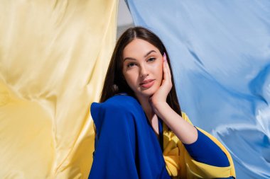 pretty ukrainian woman in stylish color block clothing posing near blue and yellow flag