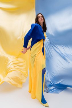 full length of patriotic ukrainian young woman in stylish clothing posing near blue and yellow fabric