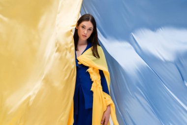 brunette ukrainian young woman in fashionable clothing posing near blue and yellow flag clipart