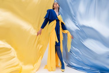 full length of patriotic ukrainian model in fashionable outfit posing near blue and yellow fabric