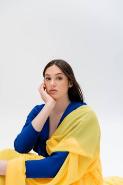 pretty ukrainian young woman in blue and yellow outfit looking at camera isolated on grey