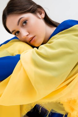 tender ukrainian young woman in blue and yellow outfit looking at camera isolated on grey