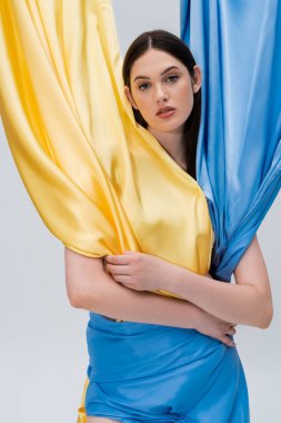 sensual young ukrainian woman in blue and yellow dress posing isolated on grey