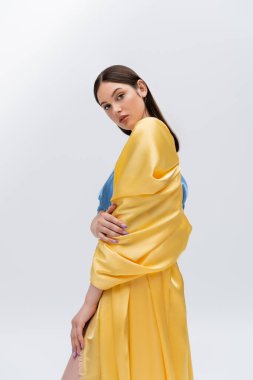sensual young ukrainian model in blue and yellow dress posing while looking at camera isolated on grey