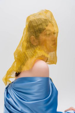 young ukrainian woman woman with yellow drapery covering face looking away isolated on grey