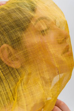 portrait of young ukrainian woman woman with yellow drapery covering face looking away isolated on grey
