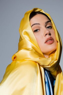 young ukrainian woman in yellow silk headscarf looking at camera isolated on grey