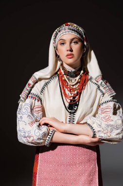 young ukrainian woman in traditional shirt with ornament and red beads posing on black