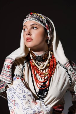 brunette ukrainian woman in traditional shirt with ornament and red beads posing isolated on black