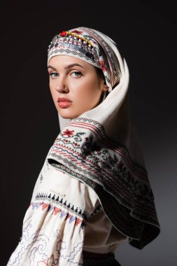 young ukrainian woman in traditional shirt with ornament looking at camera isolated on black