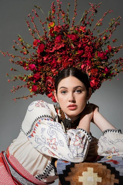 portrait of young ukrainian woman in traditional clothes and floral wreath with red berries isolated on grey