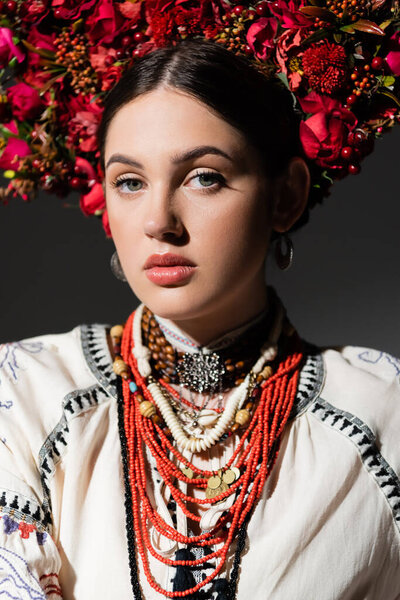 portrait of brunette and young ukrainan woman in floral wreath with red berries isolated on dark grey