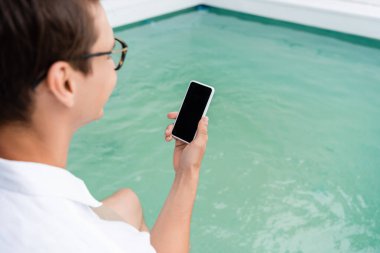 Bulanık havuz kenarında boş ekranlı, cep telefonu tutan bulanık bir adam.