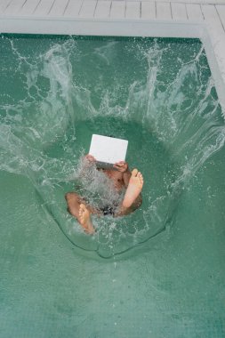 top view of freelance with laptop falling in pool with turquoise water