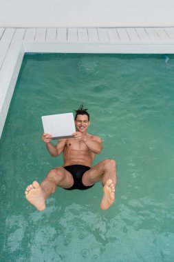 top view of cheerful man falling in pool with laptop  
