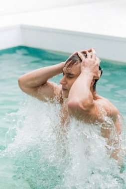 man with closed eyes touching wet hair while bathing in pool