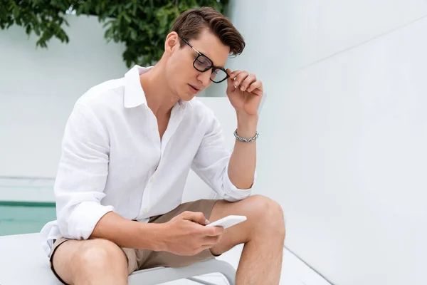 Pria Menyesuaikan Kacamata Sambil Mengobrol Pada Ponsel Luar Ruangan — Stok Foto