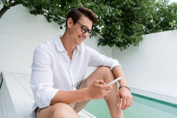 Pleased Man Eyeglasses Chatting Smartphone Pool Outdoors — стоковое фото
