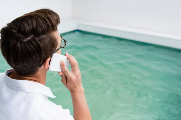 Man Eyeglasses Talking Mobile Phone Blurred Pool Turquoise Water — стоковое фото