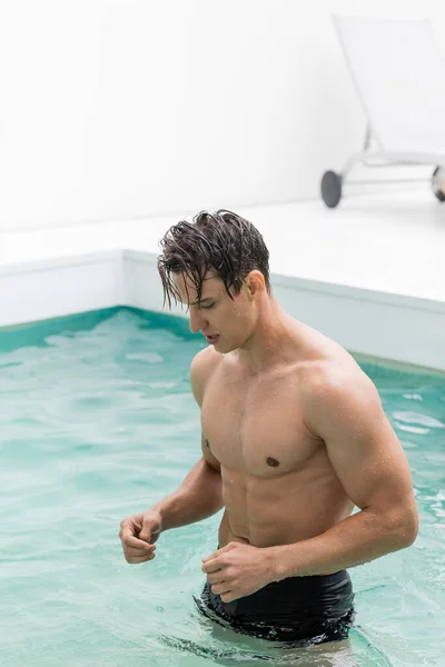 wet man with muscular torso in pool with clear turquoise water