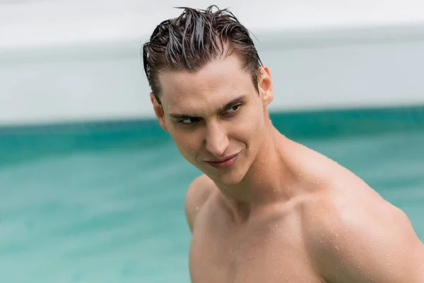 man with wet hair looking away near blurred pool