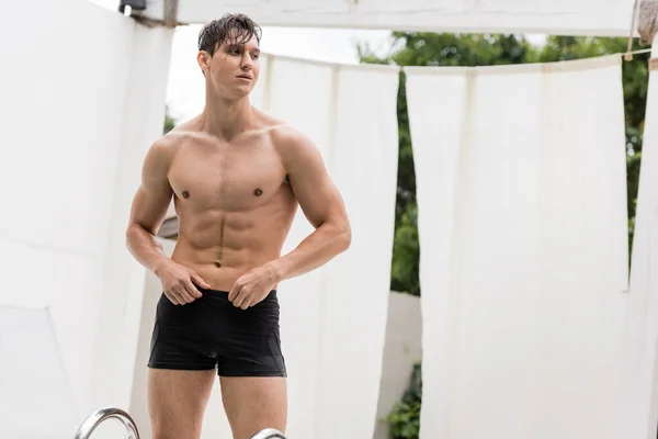 wet sportive man in swimming trunks looking away outdoors