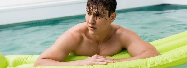 wet man looking away near swimming mattress in blurred pool, banner