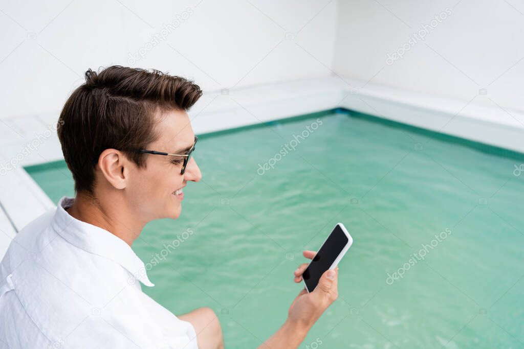 smiling man having video call on smartphone near pool with turquoise water
