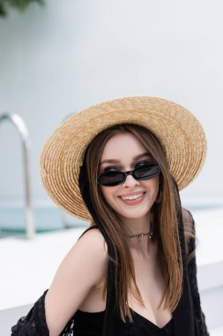 Mayo ve güneş gözlüklü, gülümseyen ve şık bir kadın tatil köyüne bakıyor. 