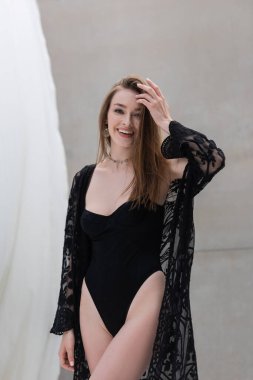 Positive woman in stylish swimsuit looking at camera at resort 