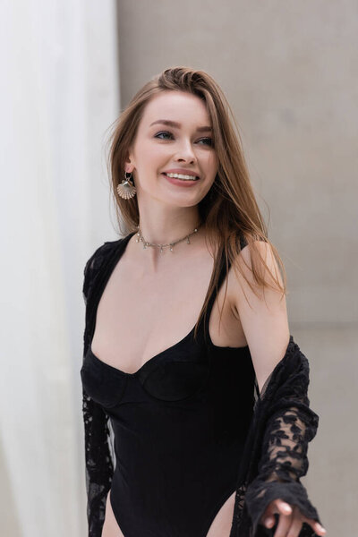 Happy brunette woman in swimsuit and guipure robe looking away at resort 