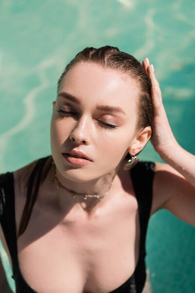 top view of pretty young woman with closed eyes and wet hair swimming in pool 