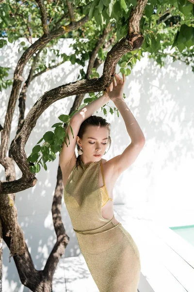 Stylová Mladá Žena Zlatých Šatech Pózuje Blízkosti Stromu Zelenými Listy — Stock fotografie