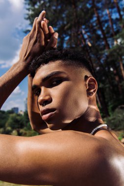 Boncuklu ve piercingli Afro-Amerikan adam portresi. Elleri başının üstünde poz veriyor.