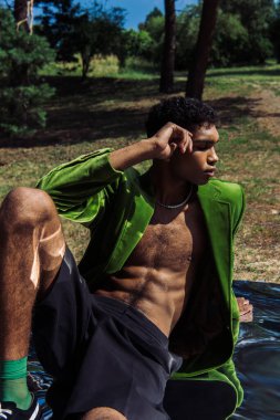 african american man with closed eyes sitting in green blazer on mirror surface in park