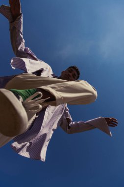 bottom view of african american man in trendy clothes under blue and clear sky
