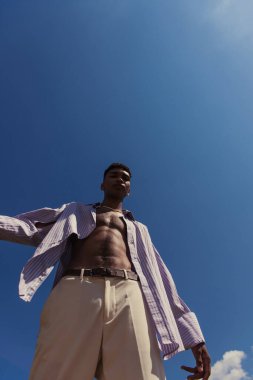 low angle view of young african american man in summer clothes under cloudless sky