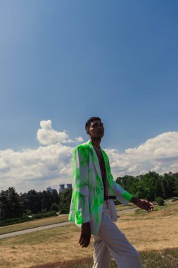 young african american man in green and white blazer walking in field near park