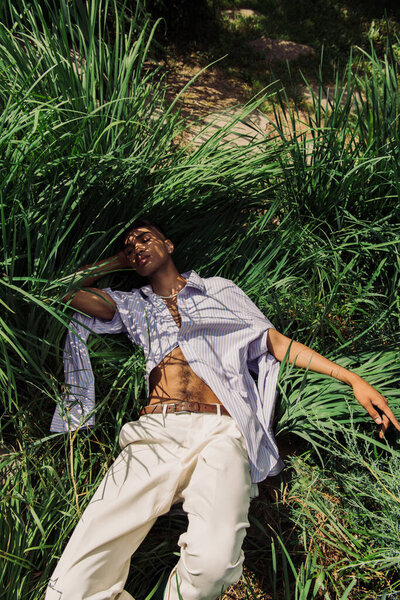 high angle view of stylish african american man with closed eyes relaxing on green grass 