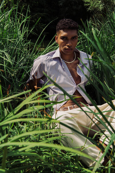 african american man in blue shirt and beads looking at camera on green grass